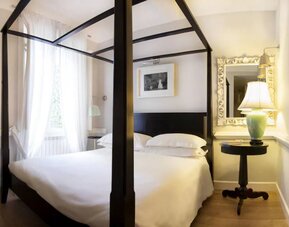 Guest room featuring a four-poster bed, hardwood flooring, sheer curtains, and elegant furnishings at Cellai Boutique Hotel.