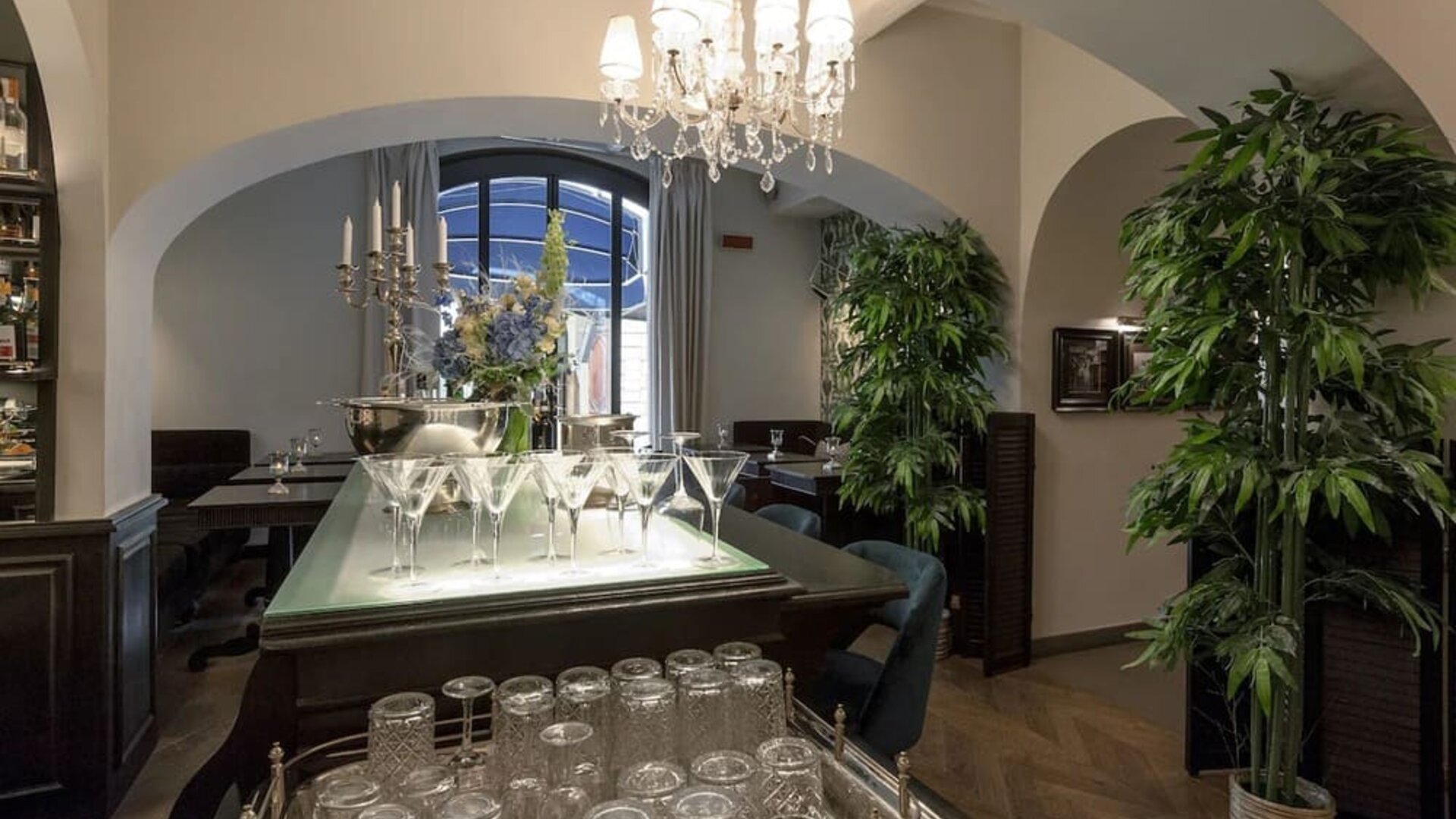 Bar area featuring crystal chandeliers, arched entryways, elegant glassware displays, and contemporary lounge seating at Cellai Boutique Hotel.
