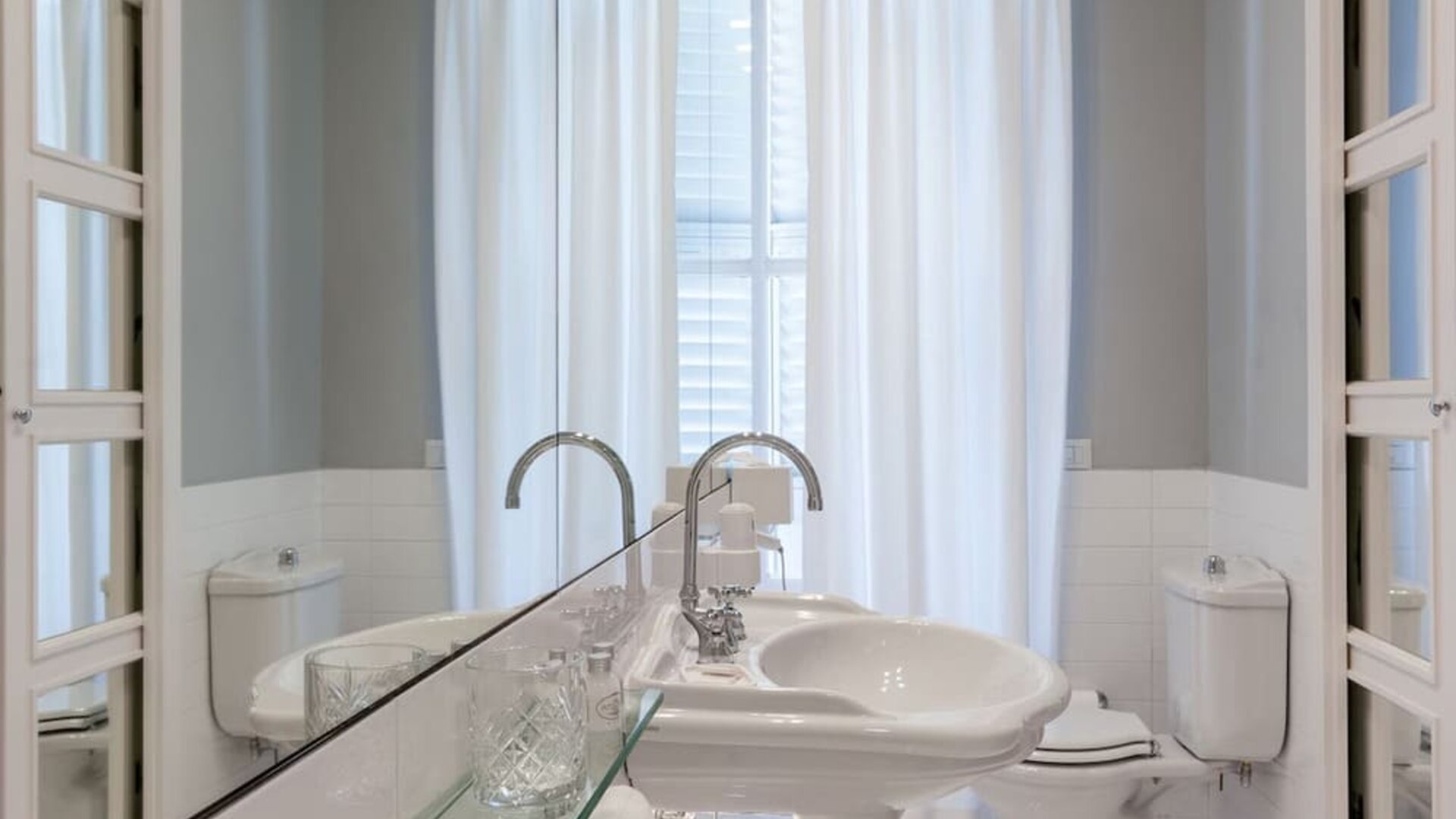 Bathroom featuring a pedestal sink, oversized mirror, bright natural light, and classic European design at Cellai Boutique Hotel.