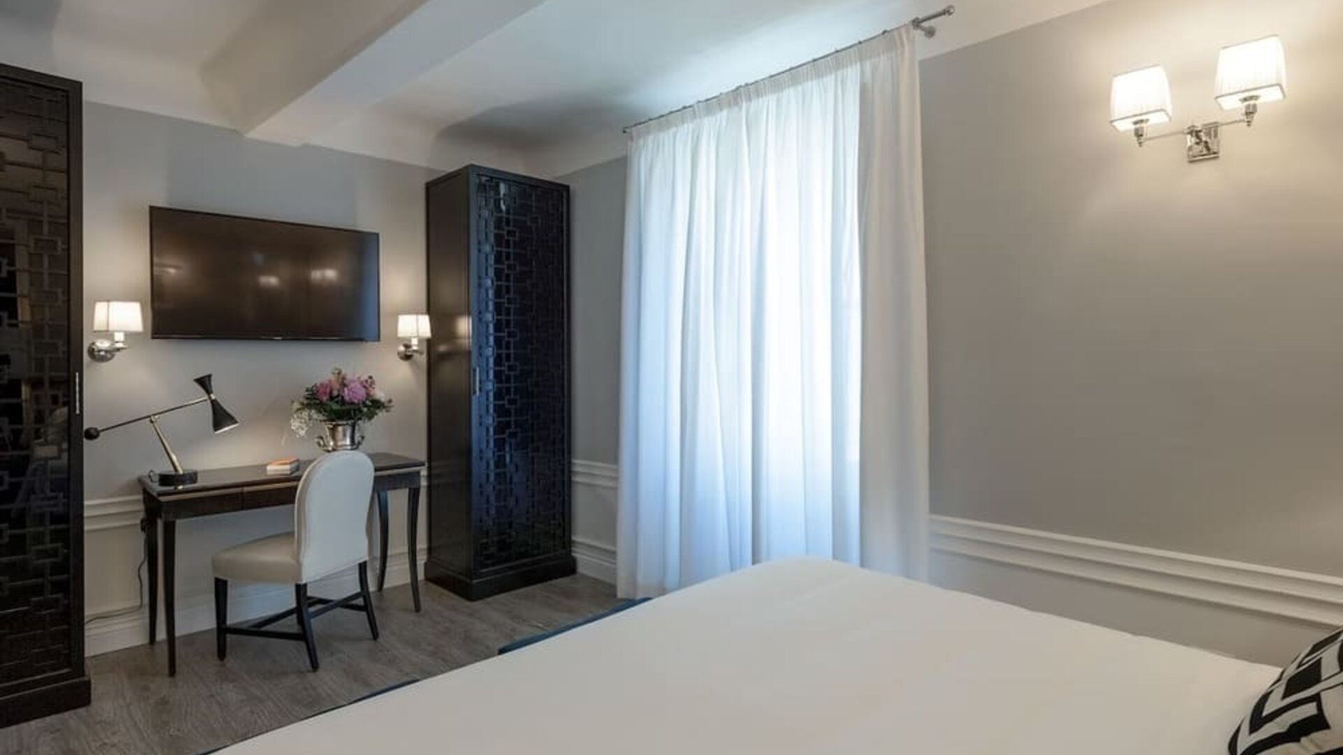 In-room workspace featuring a writing desk, upholstered chair, wall-mounted television, and contemporary furnishings at Cellai Boutique Hotel.