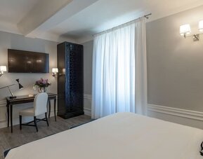 In-room workspace featuring a writing desk, upholstered chair, wall-mounted television, and contemporary furnishings at Cellai Boutique Hotel.