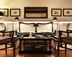 Seating area featuring upholstered chairs, warm lighting, framed artwork, and a classic lounge setting at Cellai Boutique Hotel.
