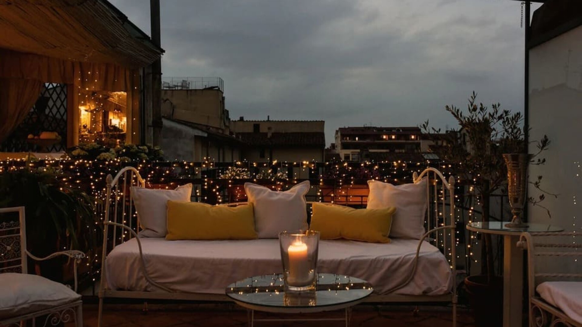 Outdoor patio featuring cushioned seating, candlelight, decorative string lights, and rooftop views at Cellai Boutique Hotel.