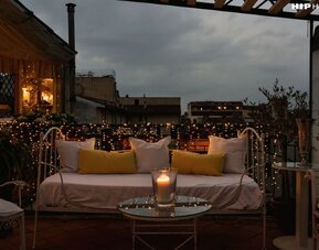 Outdoor patio featuring cushioned seating, candlelight, decorative string lights, and rooftop views at Cellai Boutique Hotel.