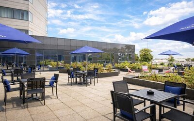 Hotel outdoor terrace with tables, chairs, landscaped planters and open views toward the nearby airport.