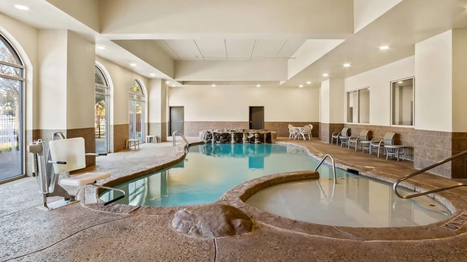 Indoor swimming pool and adjacent whirlpool spa with accessible entry and waterfall features at Comfort Suites Frisco.