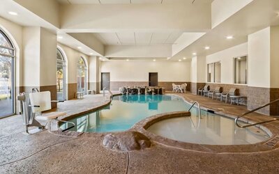 Indoor swimming pool and adjacent whirlpool spa with accessible entry and waterfall features at Comfort Suites Frisco.