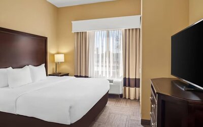 Standard king room with a flat-screen television, dresser, bedside table, and window seating area at Comfort Suites Frisco.