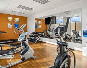Hotel gym with treadmills, elliptical machines, dumbbells, and mirrored walls at Comfort Suites Frisco.