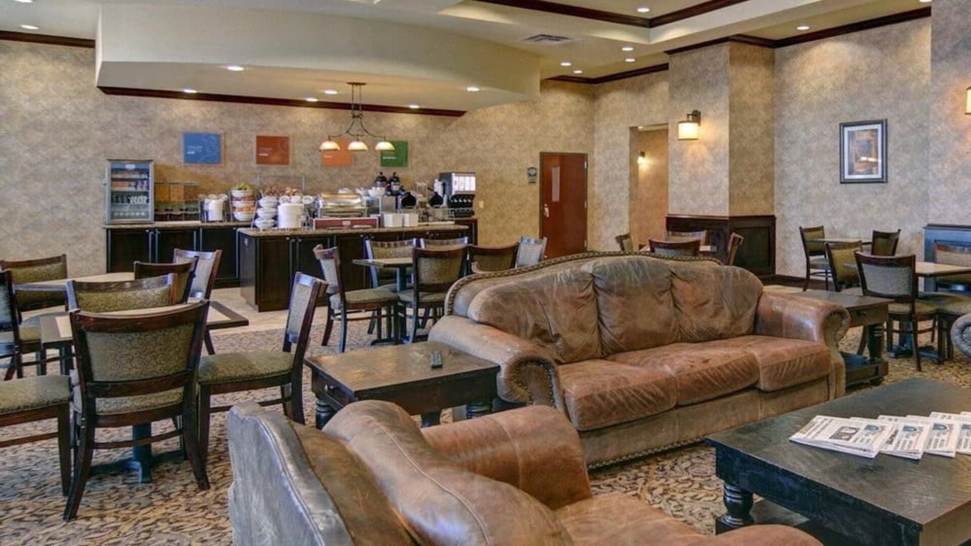 Breakfast and lounge area featuring comfortable leather seating, dining tables, and a self-serve breakfast station at Comfort Suites Frisco.