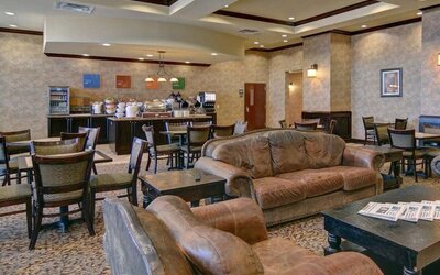 Breakfast and lounge area featuring comfortable leather seating, dining tables, and a self-serve breakfast station at Comfort Suites Frisco.