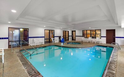 Indoor swimming pool with a hot tub, poolside seating, and accessible pool lift at Comfort Suites Vacaville-Napa Valley Area.