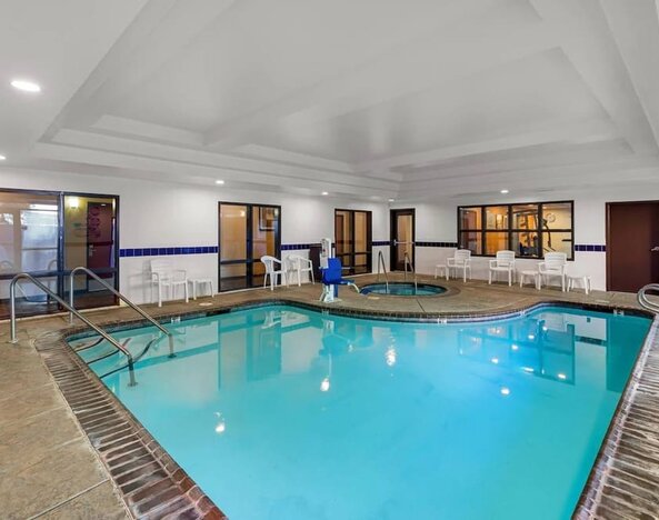 Indoor swimming pool with a hot tub, poolside seating, and accessible pool lift at Comfort Suites Vacaville-Napa Valley Area.
