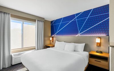 King guest room featuring a comfortable king bed, modern blue accent wall, bedside lighting, and natural light at Comfort Suites Vacaville-Napa Valley Area.