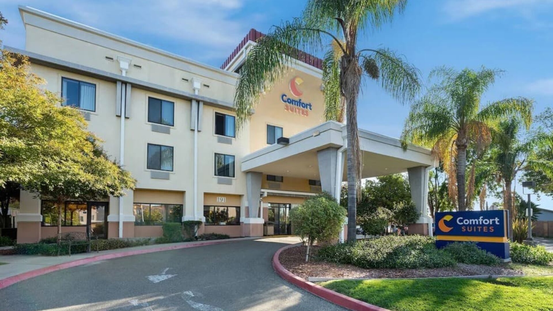 Front exterior view showcasing the covered hotel entrance, palm trees, landscaped grounds, and Comfort Suites signage at Comfort Suites Vacaville-Napa Valley Area.