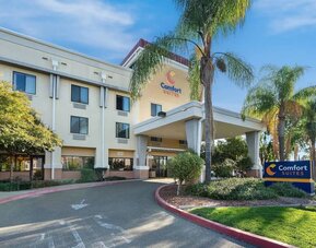 Front exterior view showcasing the covered hotel entrance, palm trees, landscaped grounds, and Comfort Suites signage at Comfort Suites Vacaville-Napa Valley Area.