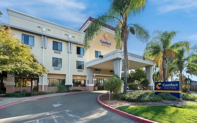 Front exterior view showcasing the covered hotel entrance, palm trees, landscaped grounds, and Comfort Suites signage at Comfort Suites Vacaville-Napa Valley Area.