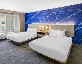 Guest room featuring two queen beds, modern blue accent décor, bedside lighting, and a large window at Comfort Suites Vacaville-Napa Valley Area.