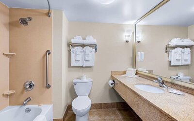 Guest bathroom featuring a bathtub and shower combination, granite vanity, large mirror, and fresh towels at Comfort Suites Vacaville-Napa Valley Area.