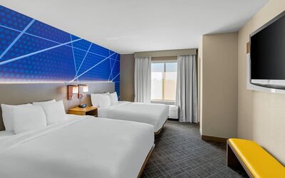 Guest room with two queen beds, modern blue accent décor, a flat-screen television, and natural light at Comfort Suites Vacaville-Napa Valley Area.