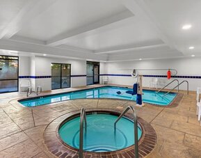 Indoor pool and hot tub area with poolside seating, handrails, and an accessible pool lift at Comfort Suites Vacaville-Napa Valley Area.