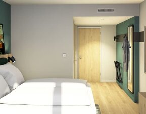 Modern hotel guest room with a large bed dressed in white linens, teal upholstered headboard, light wood flooring, wall-mounted TV, full-length mirror, and luggage rack.