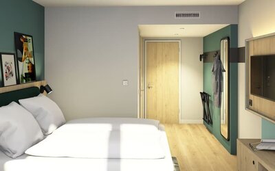 Modern hotel guest room with a large bed dressed in white linens, teal upholstered headboard, light wood flooring, wall-mounted TV, full-length mirror, and luggage rack.