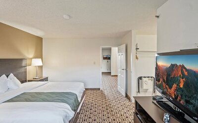 Spacious king guest room featuring a king bed, flat-screen television, storage space, and patterned carpeting at Coratel Plus Suites Wichita West Airport.