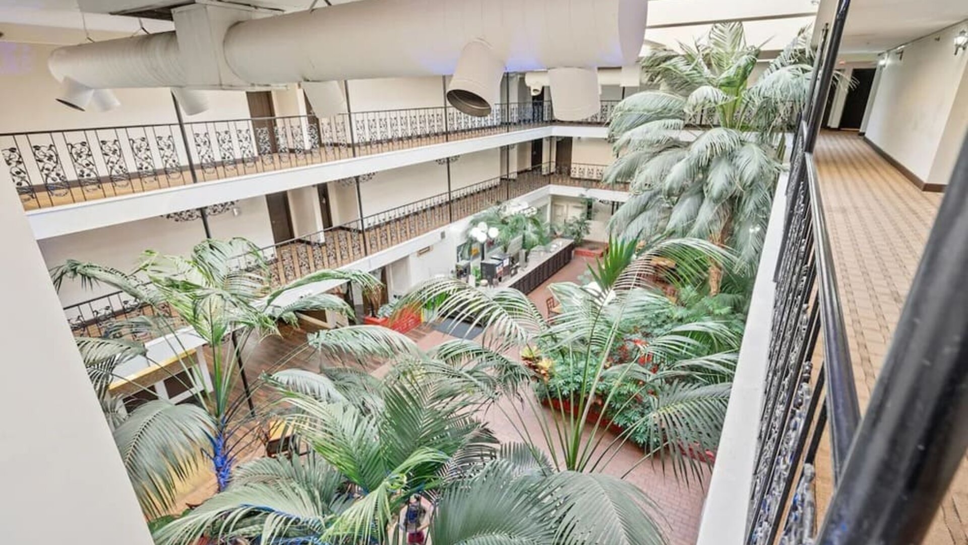 Interior atrium featuring lush tropical plants, open corridors, and decorative railings at Coratel Plus Suites Wichita West Airport.