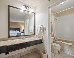 Guest bathroom featuring a granite vanity, large mirror, bathtub and shower combination, and fresh towels at Coratel Plus Suites Wichita West Airport.