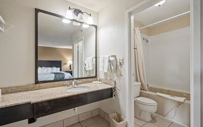 Guest bathroom featuring a granite vanity, large mirror, bathtub and shower combination, and fresh towels at Coratel Plus Suites Wichita West Airport.