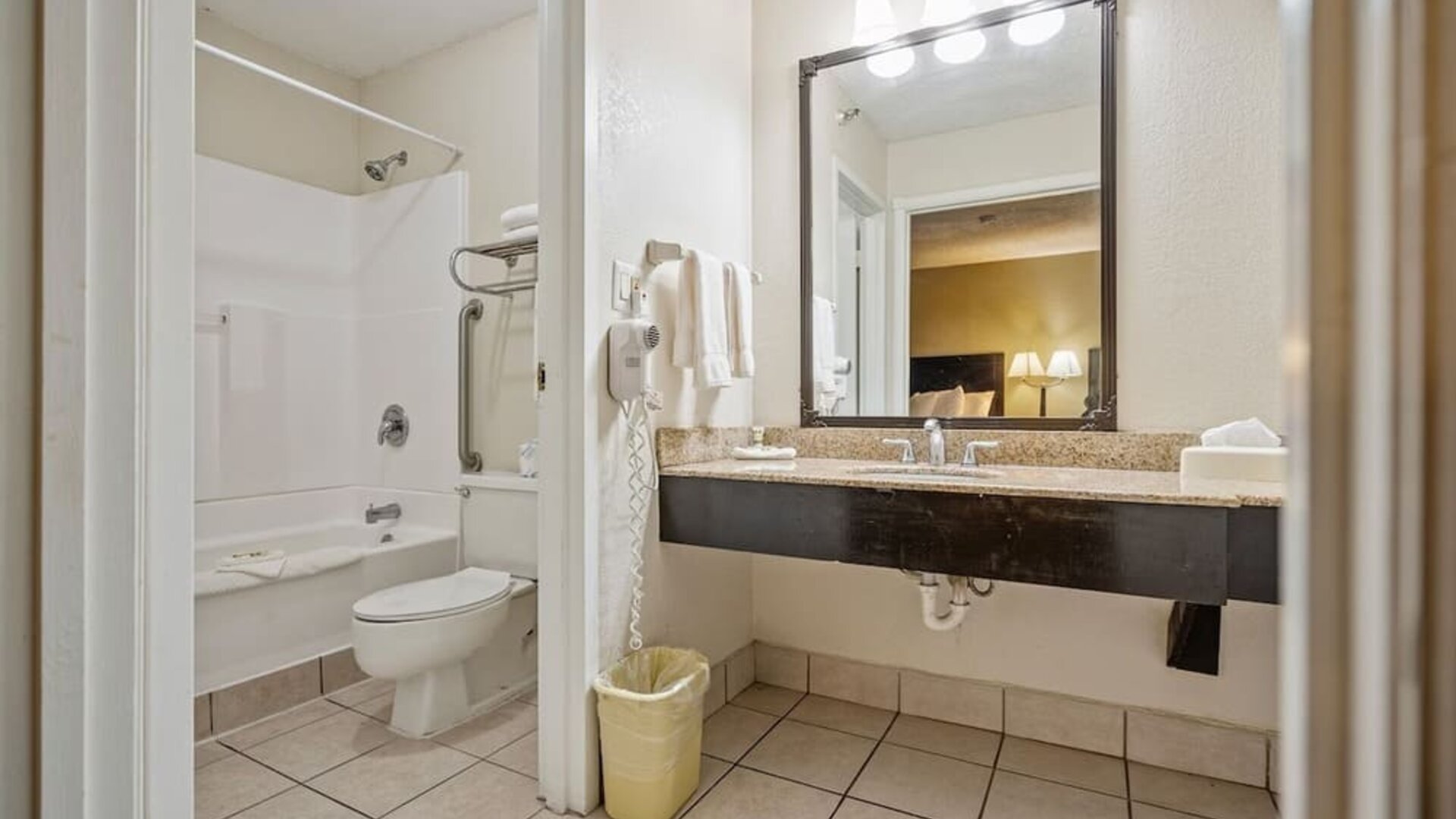 Guest bathroom featuring a bathtub and shower combination, spacious vanity, large mirror, and fresh towels at Coratel Plus Suites Wichita West Airport.