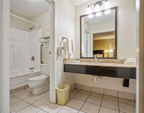 Guest bathroom featuring a bathtub and shower combination, spacious vanity, large mirror, and fresh towels at Coratel Plus Suites Wichita West Airport.