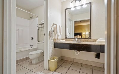 Guest bathroom featuring a bathtub and shower combination, spacious vanity, large mirror, and fresh towels at Coratel Plus Suites Wichita West Airport.