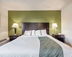 King guest room featuring a comfortable king bed, green accent wall, bedside tables, and warm lighting at Coratel Plus Suites Wichita West Airport.