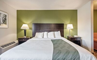 King guest room featuring a comfortable king bed, green accent wall, bedside tables, and warm lighting at Coratel Plus Suites Wichita West Airport.