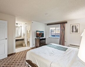 Spacious king guest room featuring a king bed, flat-screen television, large window, and convenient access to the bathroom at Coratel Plus Suites Wichita West Airport.