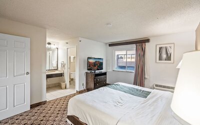 Spacious king guest room featuring a king bed, flat-screen television, large window, and convenient access to the bathroom at Coratel Plus Suites Wichita West Airport.