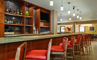Contemporary hotel bar featuring countertop seating, pendant lighting, beverage displays, and a flat-screen television at Hyatt Place San Jose Downtown.