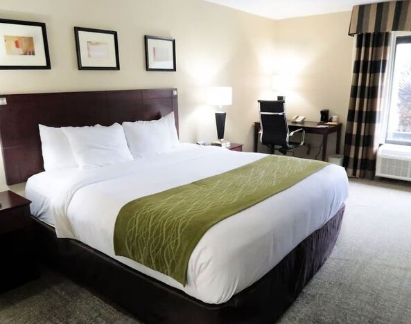 Bright king guest room featuring a king bed, work desk, chair, bedside lighting, and large window providing natural light at Comfort Inn Southwest At Westpark.