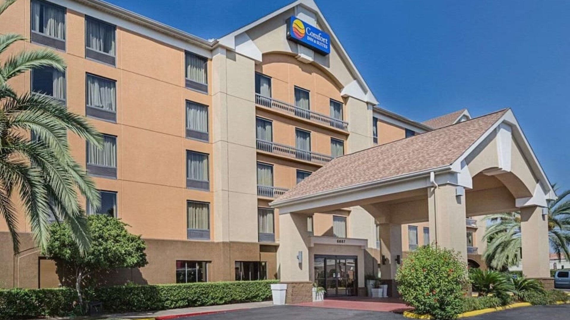 Exterior view of the multi-storey hotel featuring a covered entrance, landscaped grounds, and palm trees at Comfort Inn Southwest At Westpark.