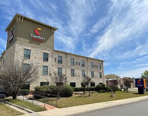 Exterior view of Comfort Suites San Antonio SeaWorld - Lackland AFB, featuring the multi-storey stone façade, landscaped grounds, and hotel signage.