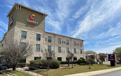 Exterior view of Comfort Suites San Antonio SeaWorld - Lackland AFB, featuring the multi-storey stone façade, landscaped grounds, and hotel signage.