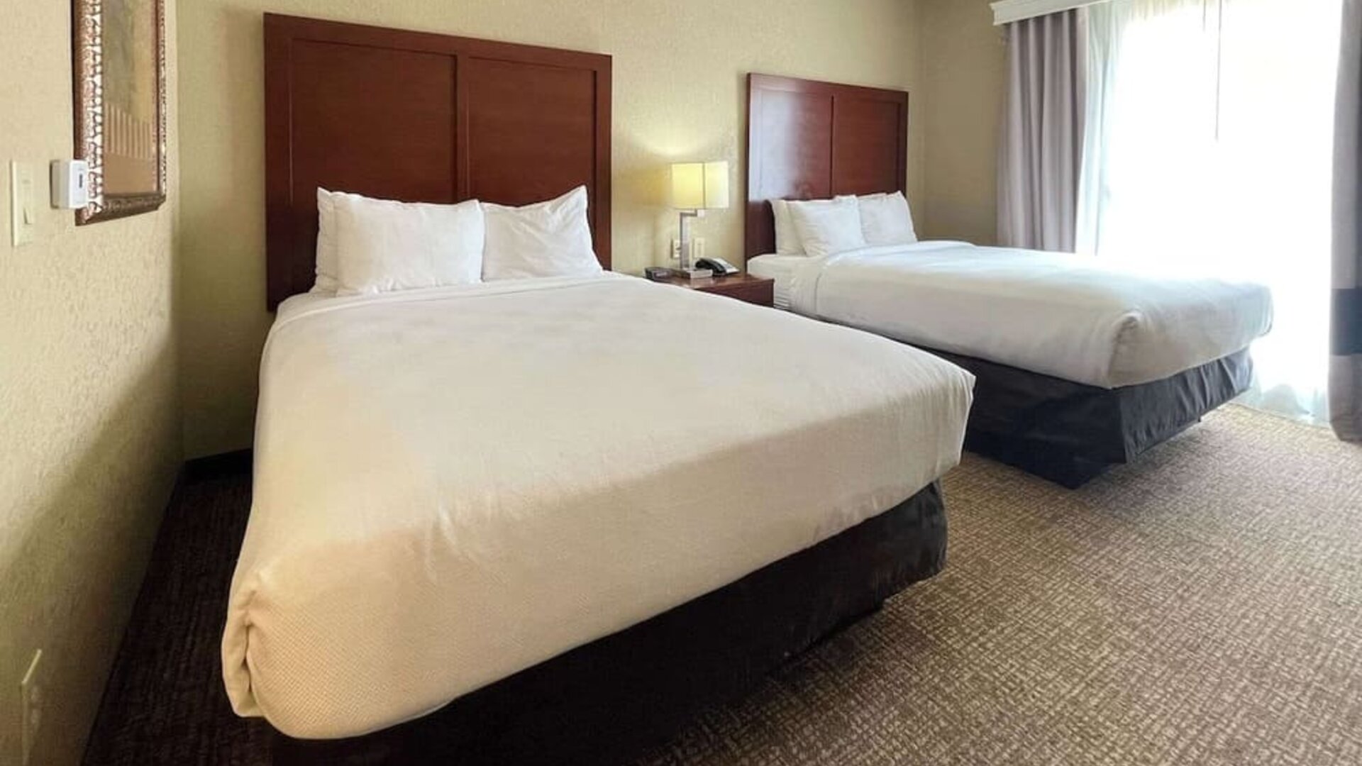 Guest room with two beds, bedside table, lamp, and natural light from a large window at Comfort Suites San Antonio SeaWorld - Lackland AFB.