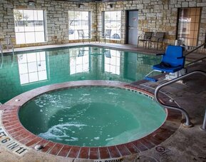 Indoor swimming pool and hot tub with accessibility lift, poolside seating, and large windows at Comfort Suites San Antonio SeaWorld - Lackland AFB.