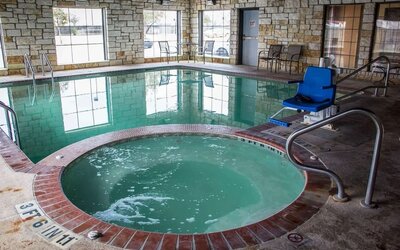 Indoor swimming pool and hot tub with accessibility lift, poolside seating, and large windows at Comfort Suites San Antonio SeaWorld - Lackland AFB.