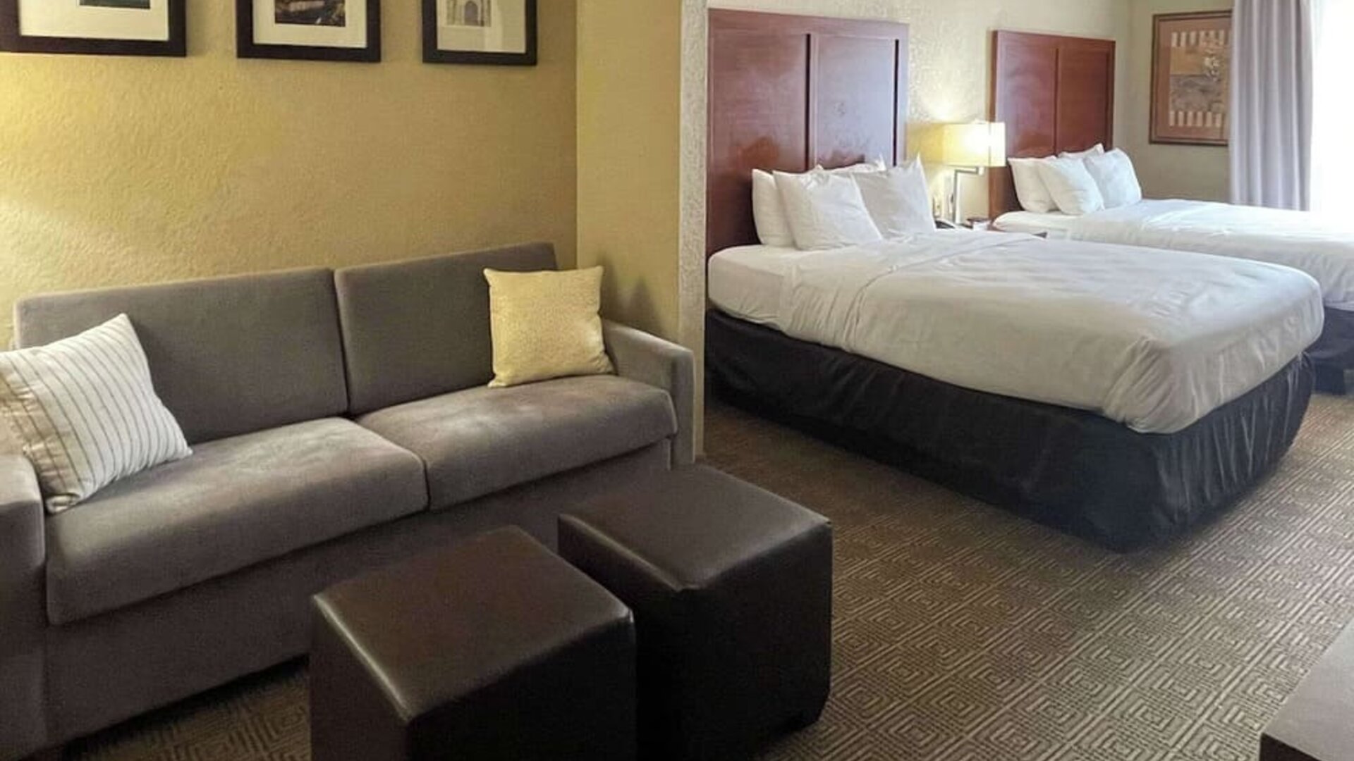 Spacious guest suite with two beds, sofa, ottomans, bedside lighting, and separate seating area at Comfort Suites San Antonio SeaWorld - Lackland AFB.