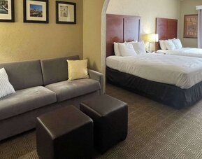 Spacious guest suite with two beds, sofa, ottomans, bedside lighting, and separate seating area at Comfort Suites San Antonio SeaWorld - Lackland AFB.