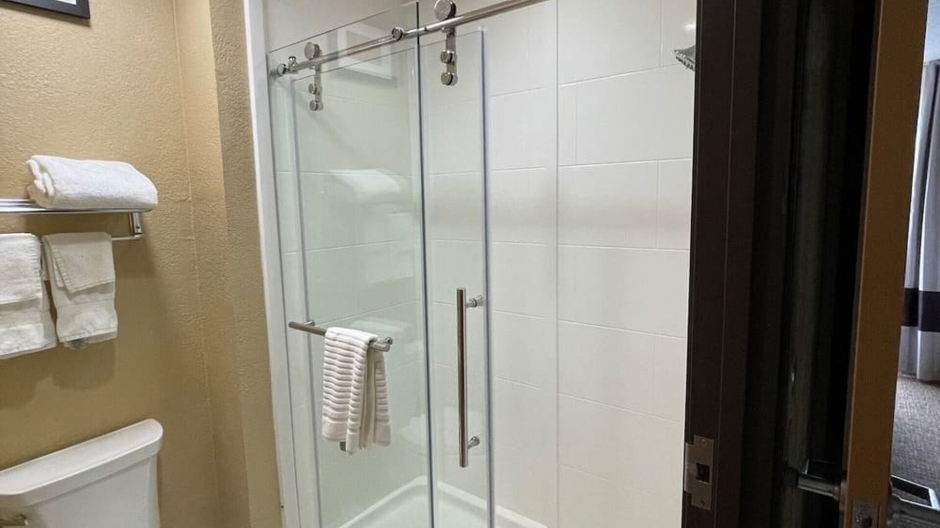 Guest bathroom with glass-enclosed walk-in shower, toilet, and fresh towels at Comfort Suites San Antonio SeaWorld - Lackland AFB.