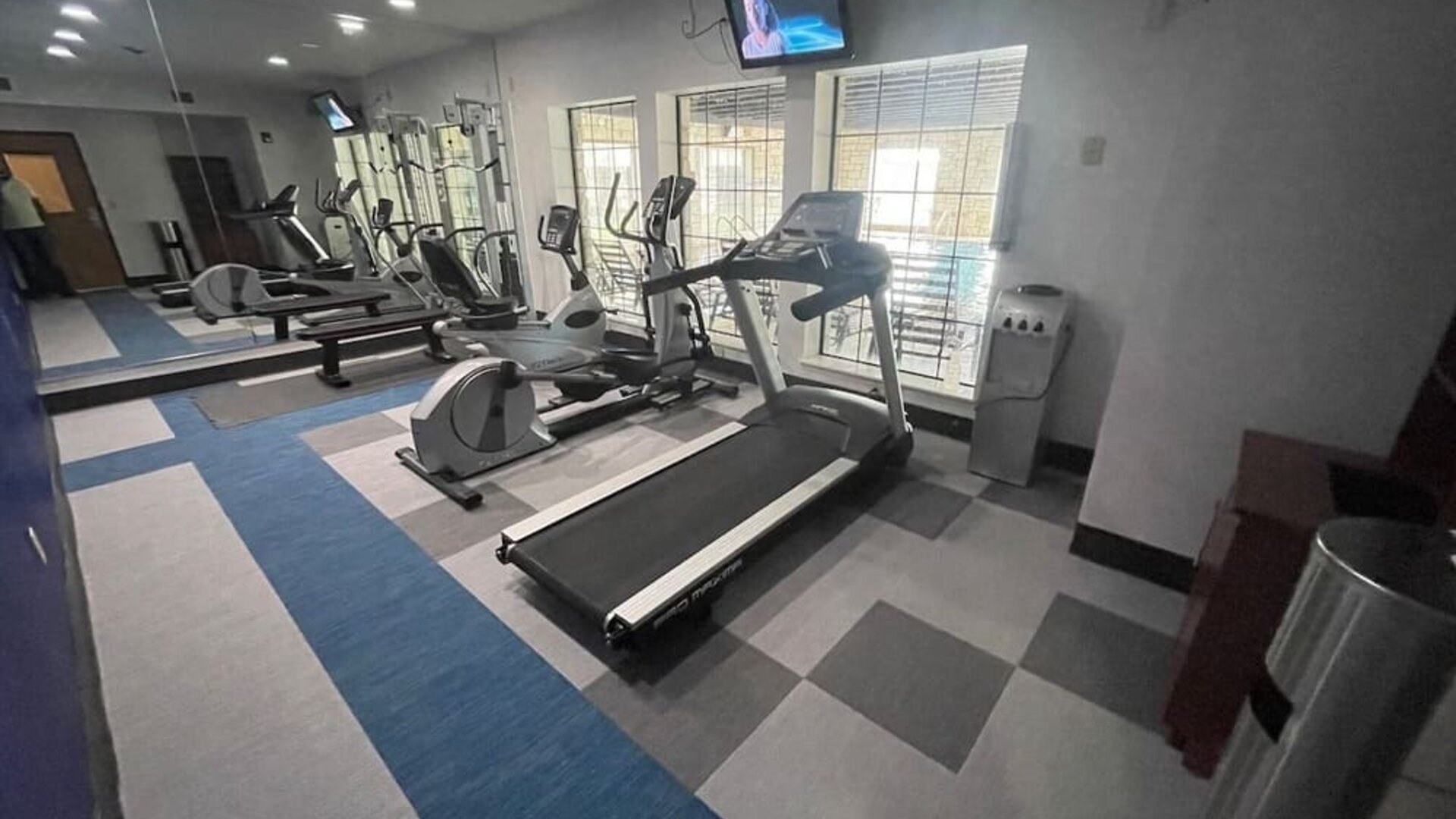 Spacious fitness centre with cardio equipment, mirrored wall, televisions, and large windows at Comfort Suites San Antonio SeaWorld - Lackland AFB.